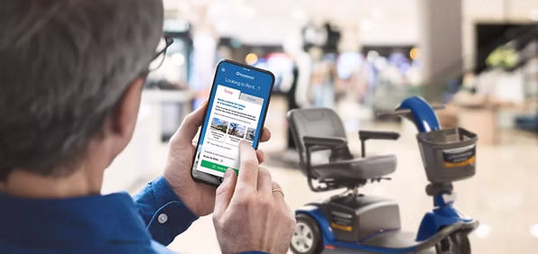 A customer using the Scootaround rental app on their phone next to a mobility scooter